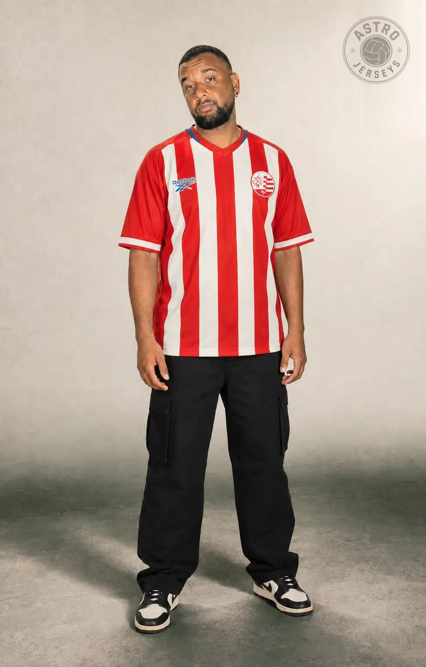 Pessoa de corpo inteiro vestindo a camisa Náutico Clássica, vermelha e branca, em estúdio de fundo neutro