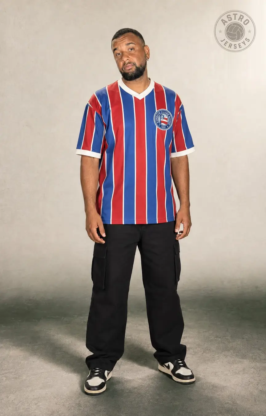 Pessoa de corpo inteiro vestindo a camisa Bahia 1988, tricolor, em estúdio de fundo neutro