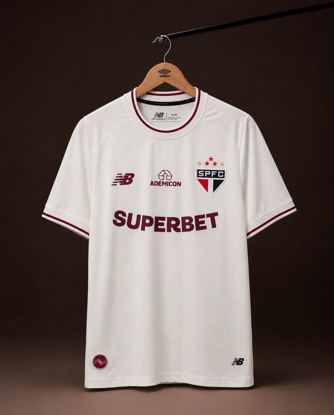 Camisa São Paulo 26/27, off-white e vinho, vista de frente em cabide sobre fundo de estudio escuro
